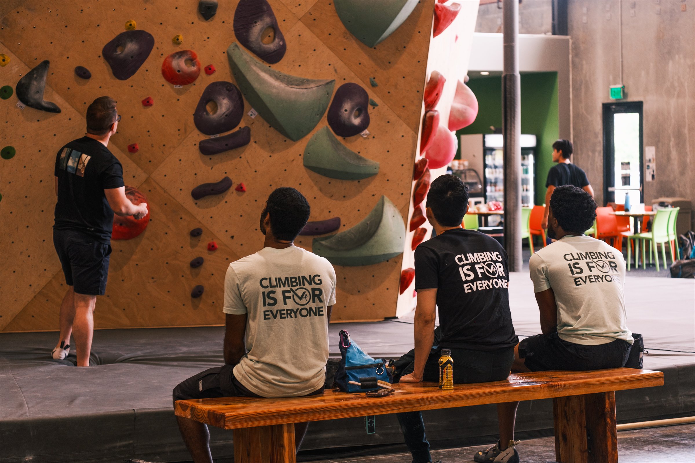 Climbers gathering beside a bouldering wall in Climbing is for Everyone shirts.